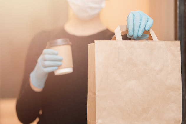 Delivery woman holding coffee and boxes cardboard in medical mask and rubber gloves. Quarantine online shopping.