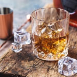 Glass of scotch whiskey with ice cubes, bottle and copper bar accessories
