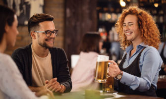 Happy waitress serving beer to a couple in a pub