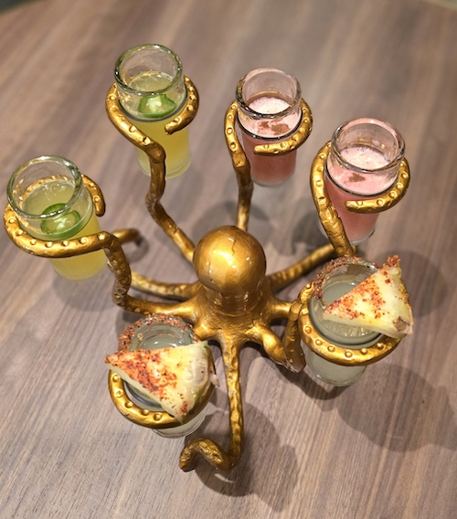 Gold octopus shaped object holding four cocktails