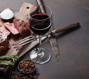 a glass of red wine next to a grilled steak